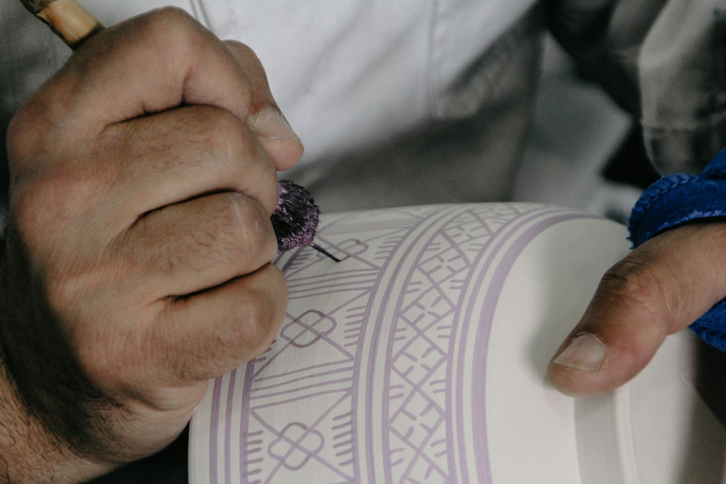 Mani che decorano un oggetto in ceramica bianca con un motivo geometrico viola.