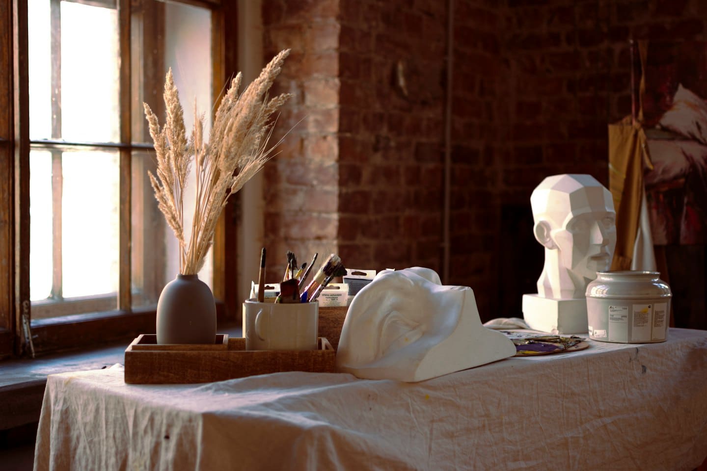 La luce della finestra dello studio dell'artista cade su un tavolo con vaso e calchi in gesso.