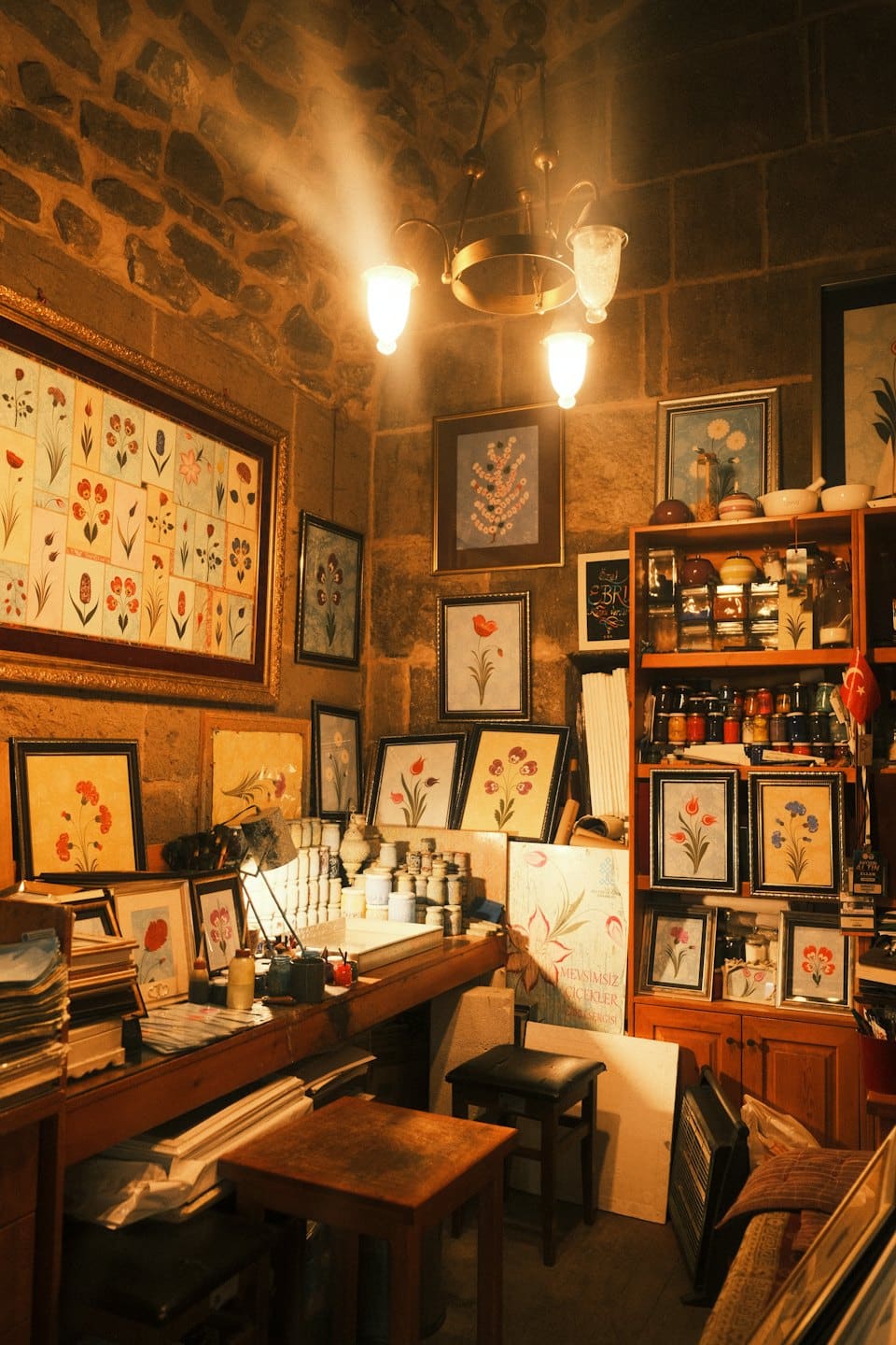 Quadri floreali incorniciati esposti in un rustico studio d'arte in pietra.
